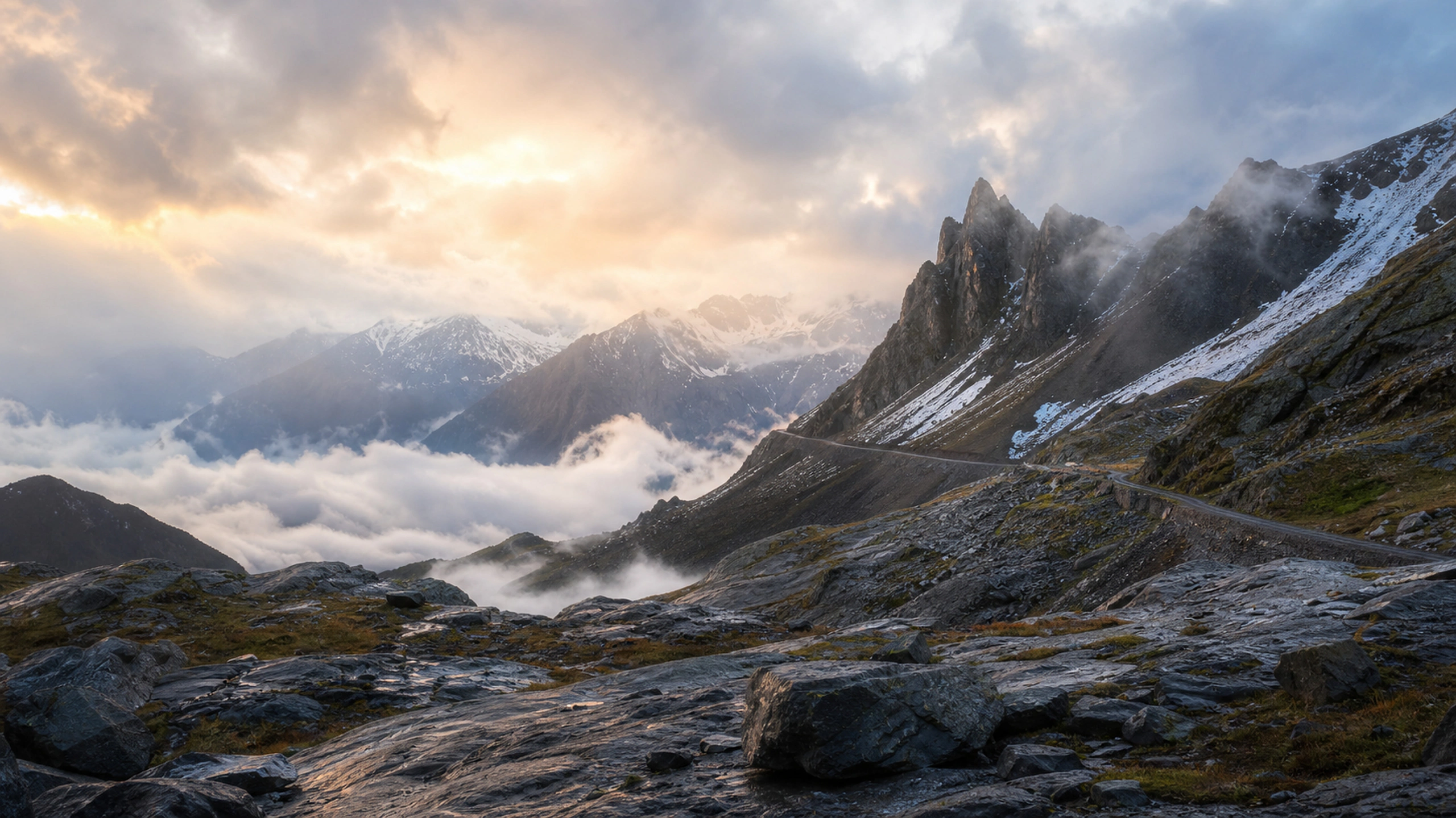 High mountain pass emerging through broken dawn cloud, wet black rocks and distant snow, original 4K nature wallpaper