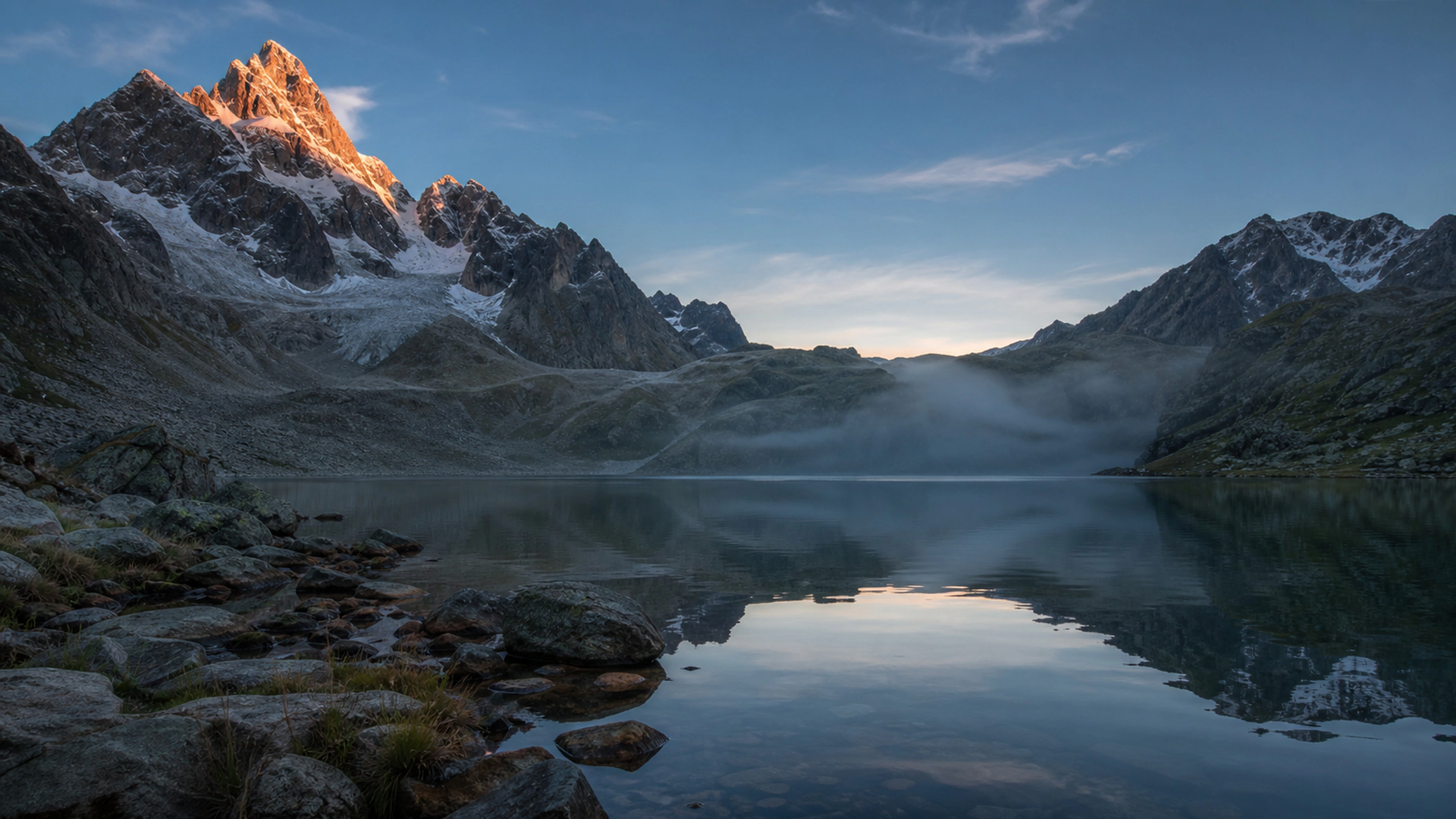 First orange light touching one snow summit above a dark still valley, original 4K mountains wallpaper