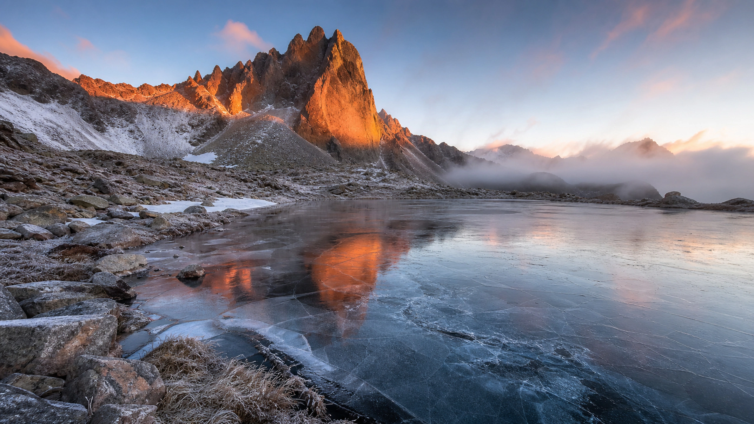 Thinly frozen tarn beneath orange-lit cliffs, natural cracks and frost texture, original 4K mountains wallpaper