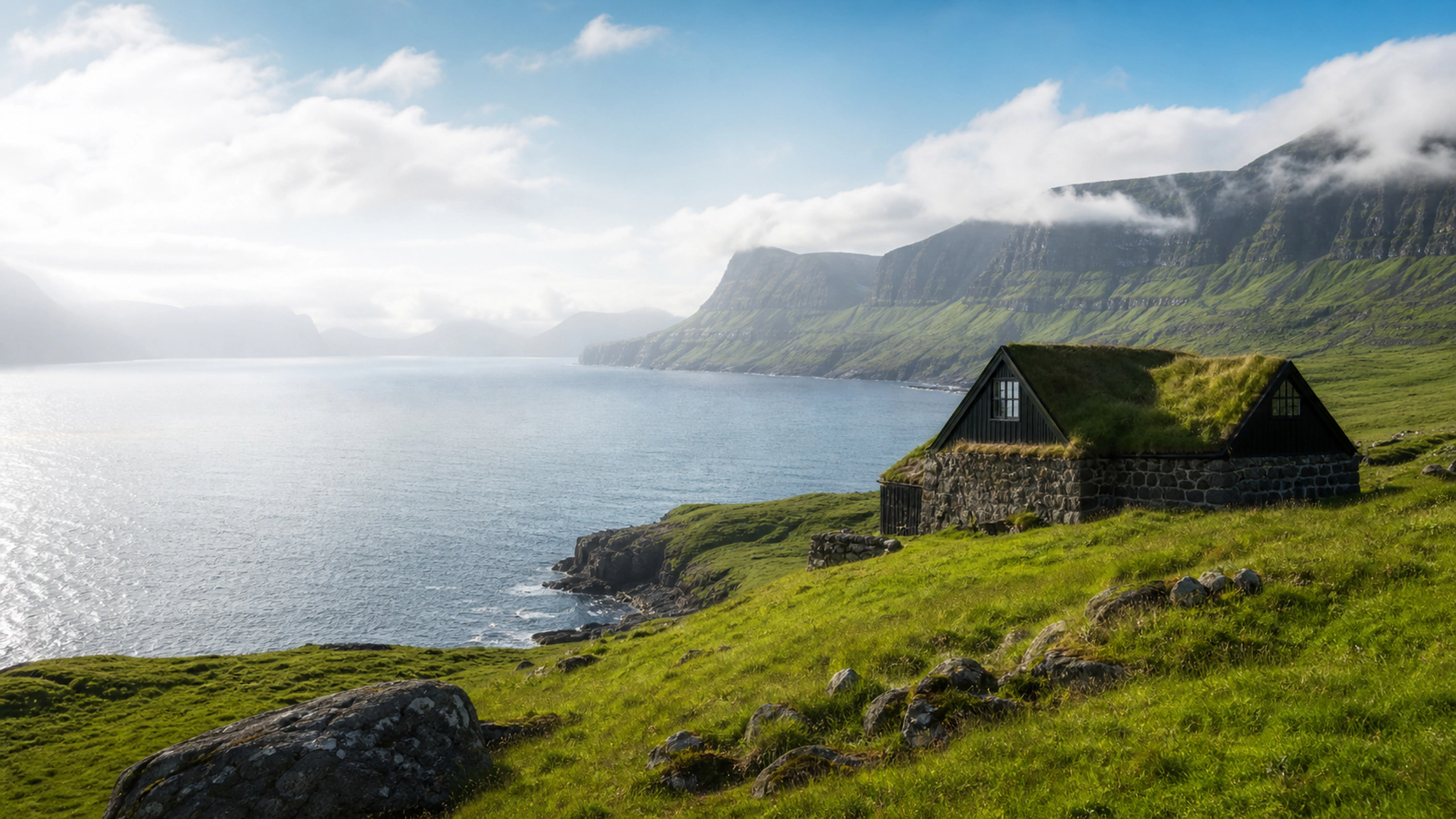 Grass-roofed cottage above a cold northern fjord, low clouds and silver water, original 4K travel wallpaper