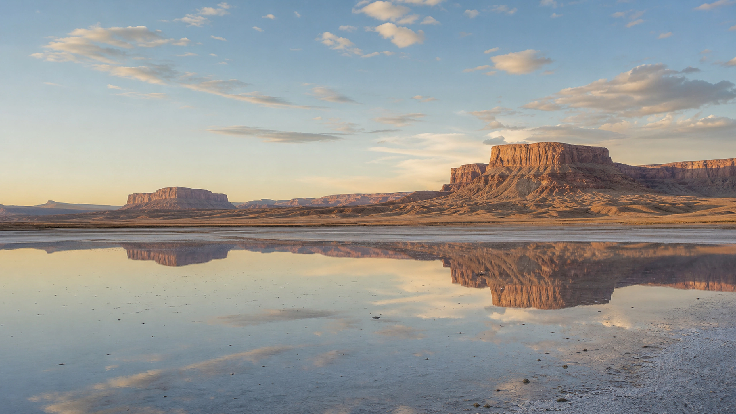 Distant mesas reflected in a thin desert salt pan beneath heat-softened afternoon light, original 4K desert wallpaper