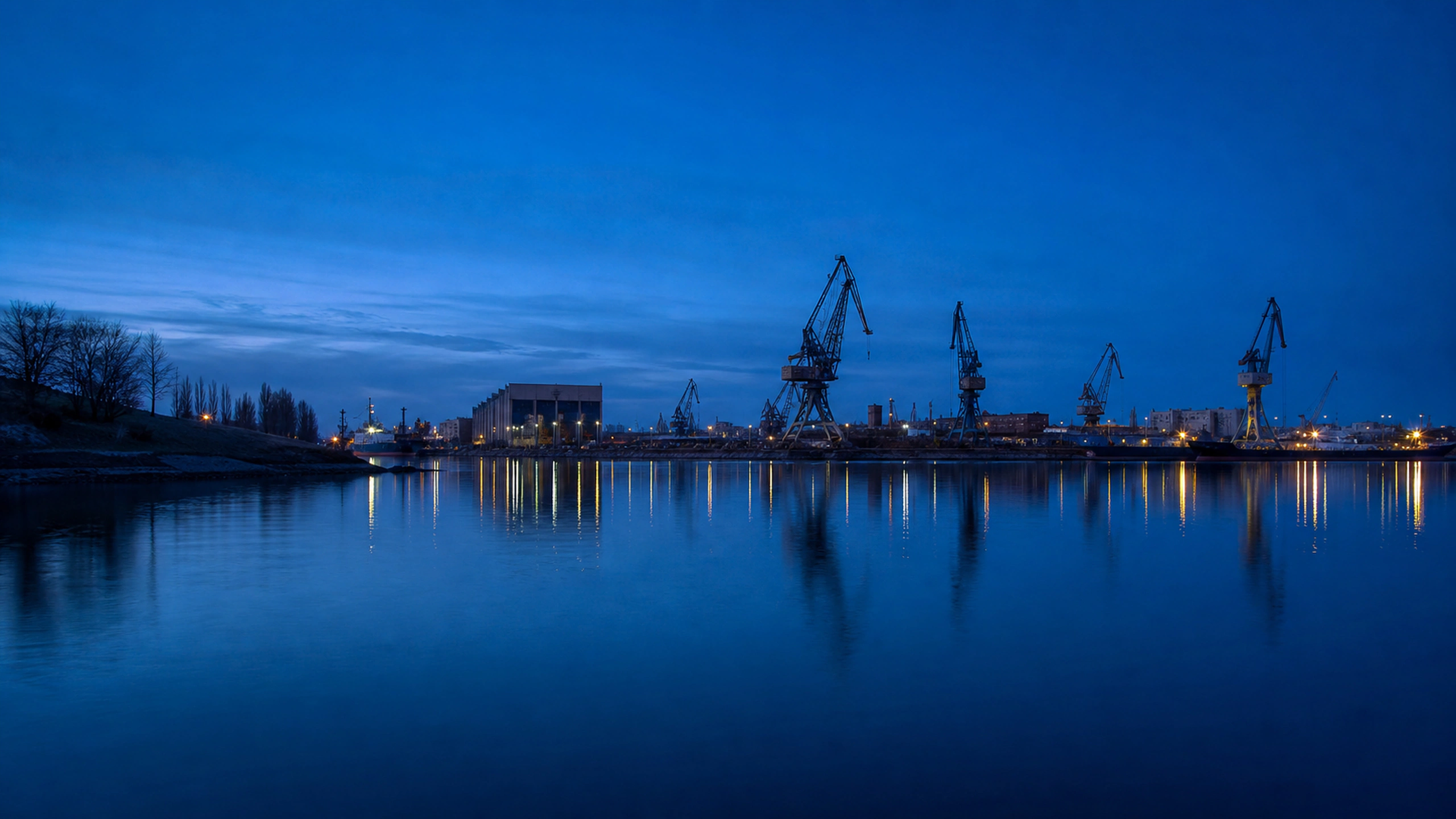 Quiet contemporary industrial harbor with cranes silhouetted against cobalt twilight, original 4K cities wallpaper