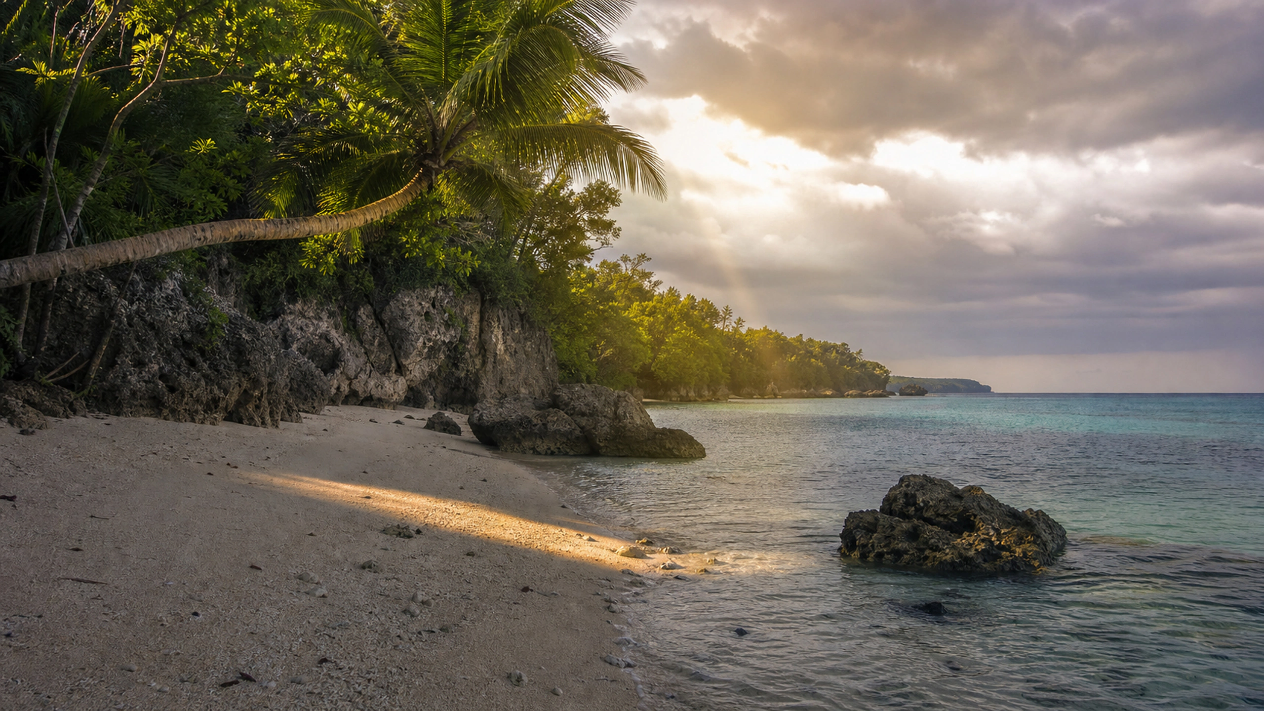 Single warm sunbeam crossing a remote beach after tropical clouds part, original 4K beaches wallpaper