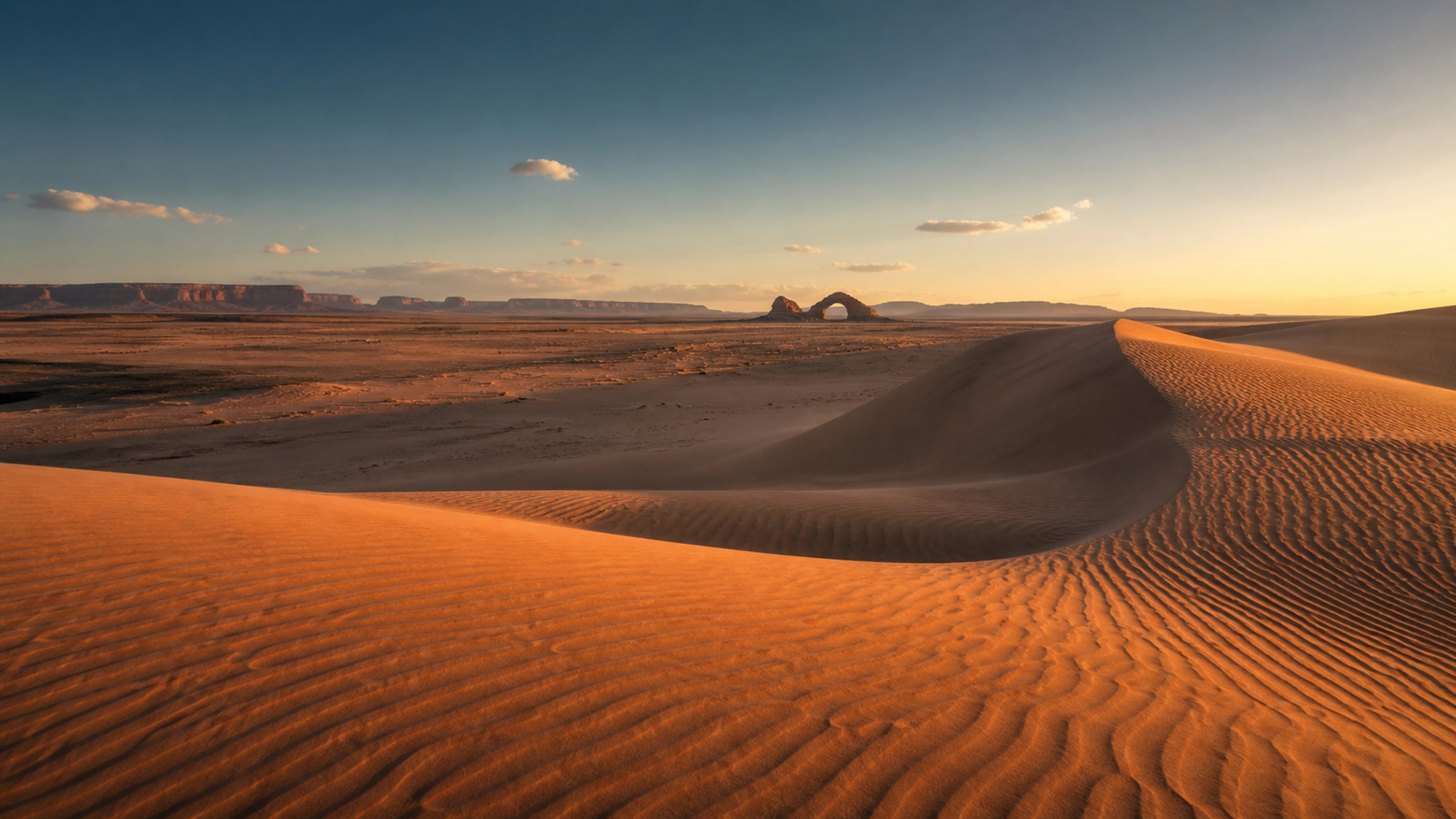 Small distant arch beyond flowing foreground dunes, low warm side light, original 4K desert wallpaper