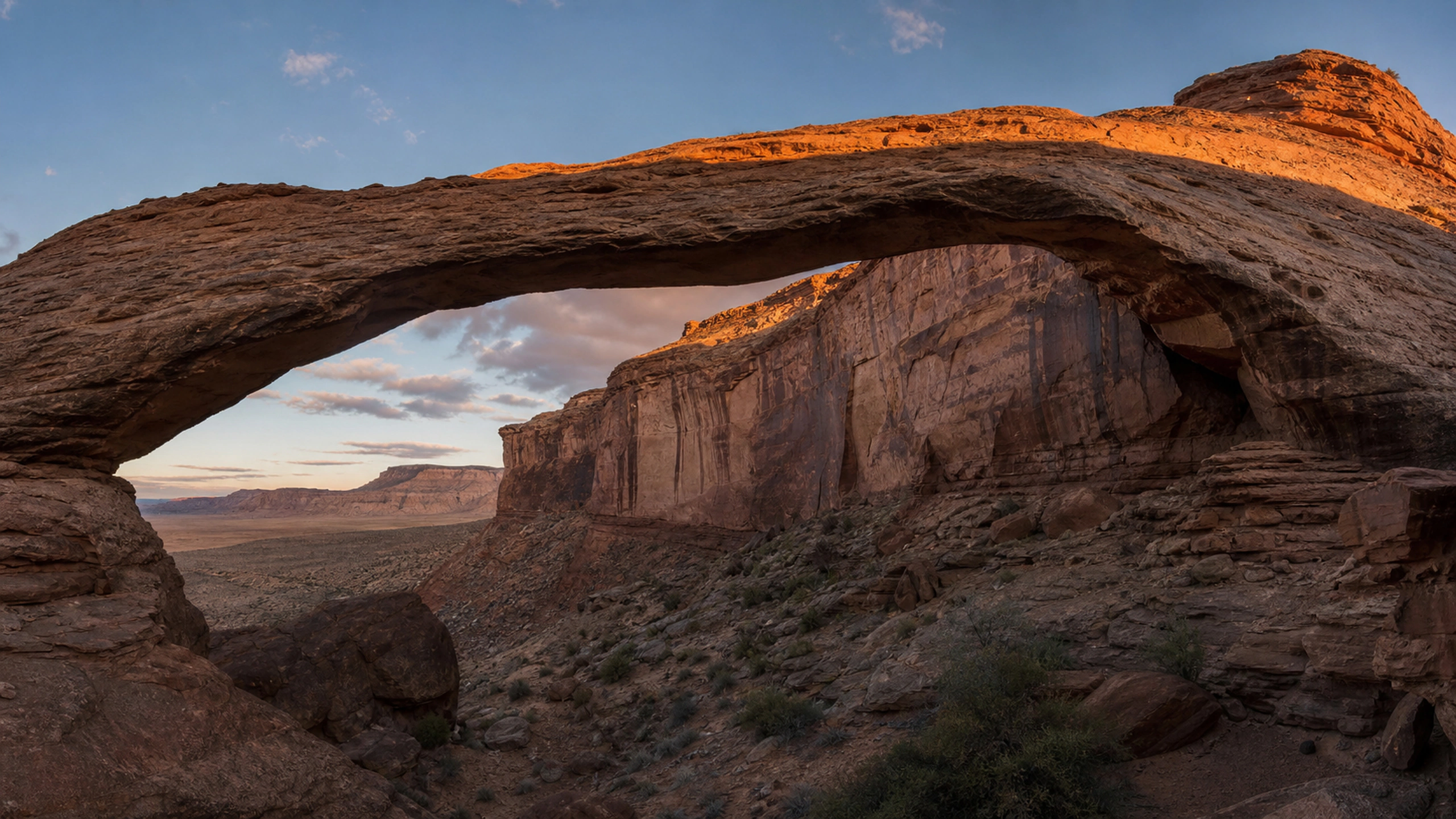 Massive arch bridging a narrow canyon with deep realistic shadow and glowing upper stone, original 4K desert wallpaper