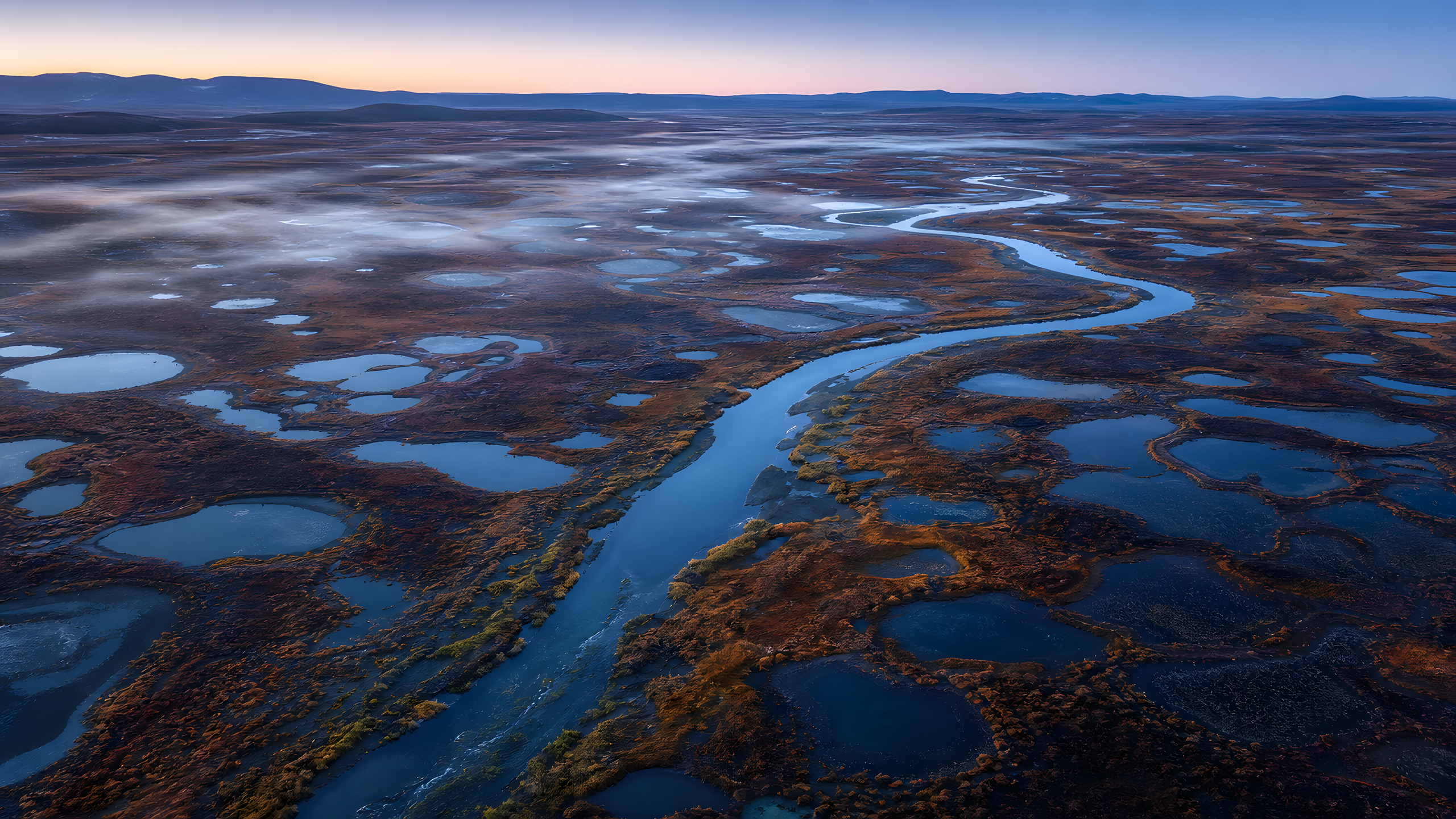 An expansive arctic tundra wetland in early autumn with russet dwarf shrubs, ochre sedges, dark thaw ponds and winding shallow channels, seen from a near-vertical aerial at quiet blue hour, original 4K nature wallpaper