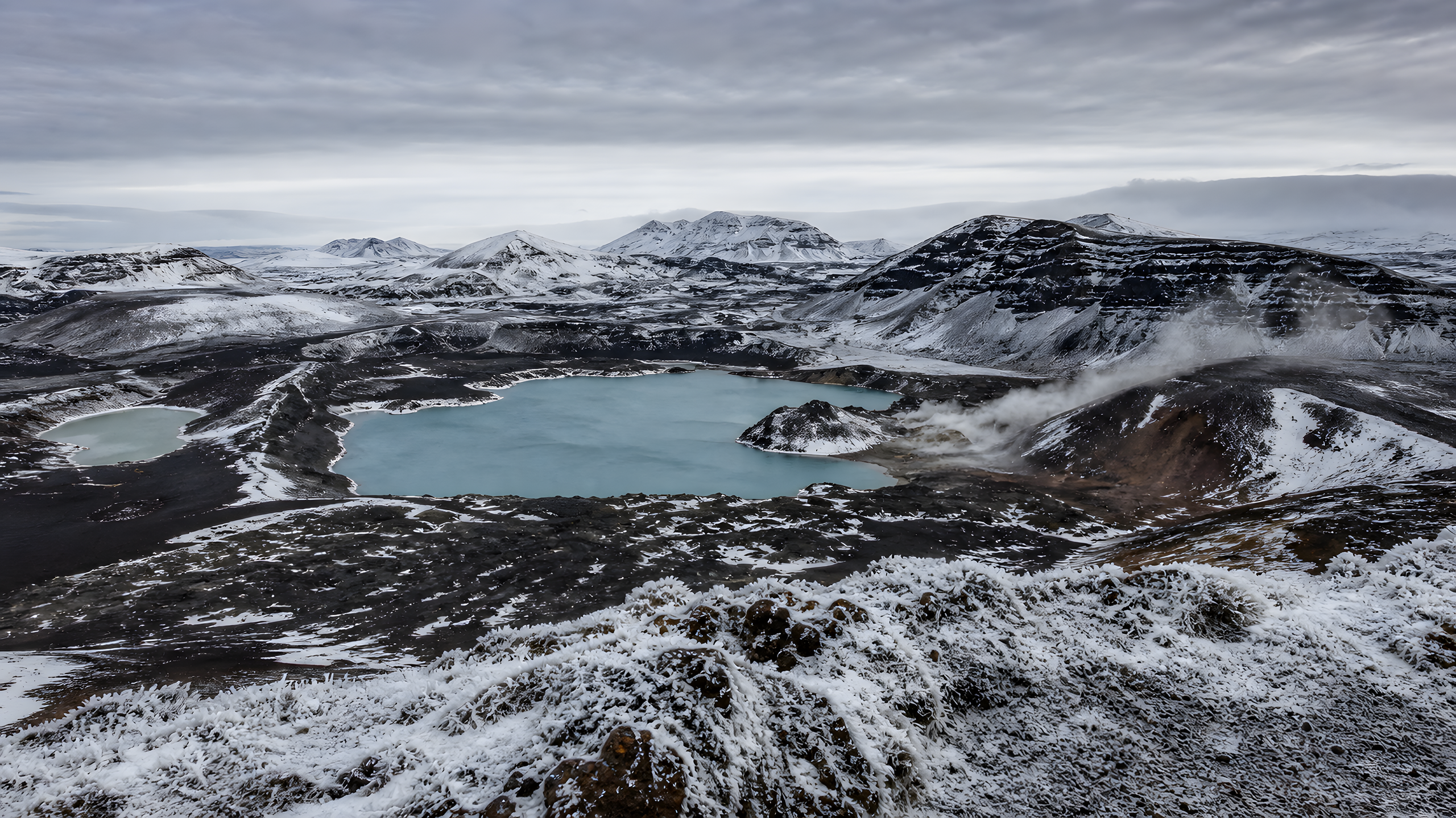 A broad unnamed volcanic caldera in winter with black lava terraces, a mineral-blue crater lake, snow ribbons and geothermal steam, viewed from a high rime-covered rim beneath textured polar overcast, original 4K nature wallpaper