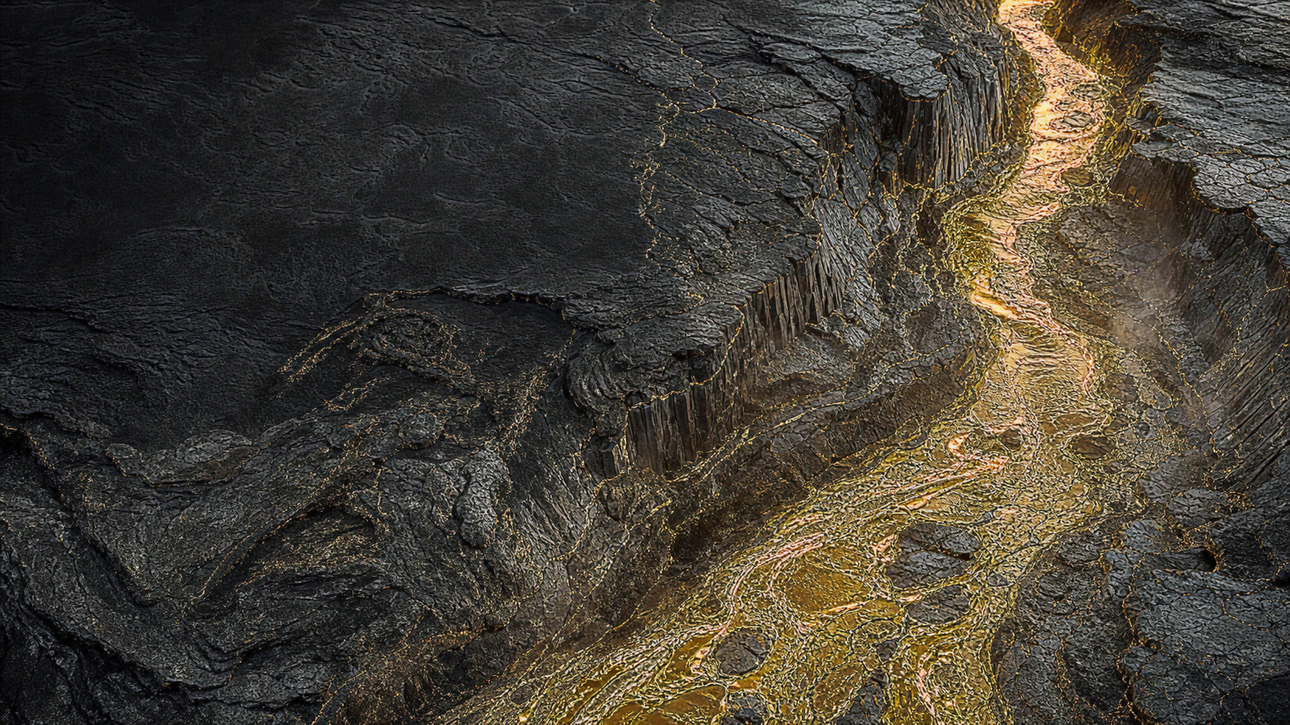 Aerial view into a black basalt canyon carrying a narrow molten-gold river, sharply layered geology and tiny cooled metallic tributaries, original 4K dark amoled wallpaper