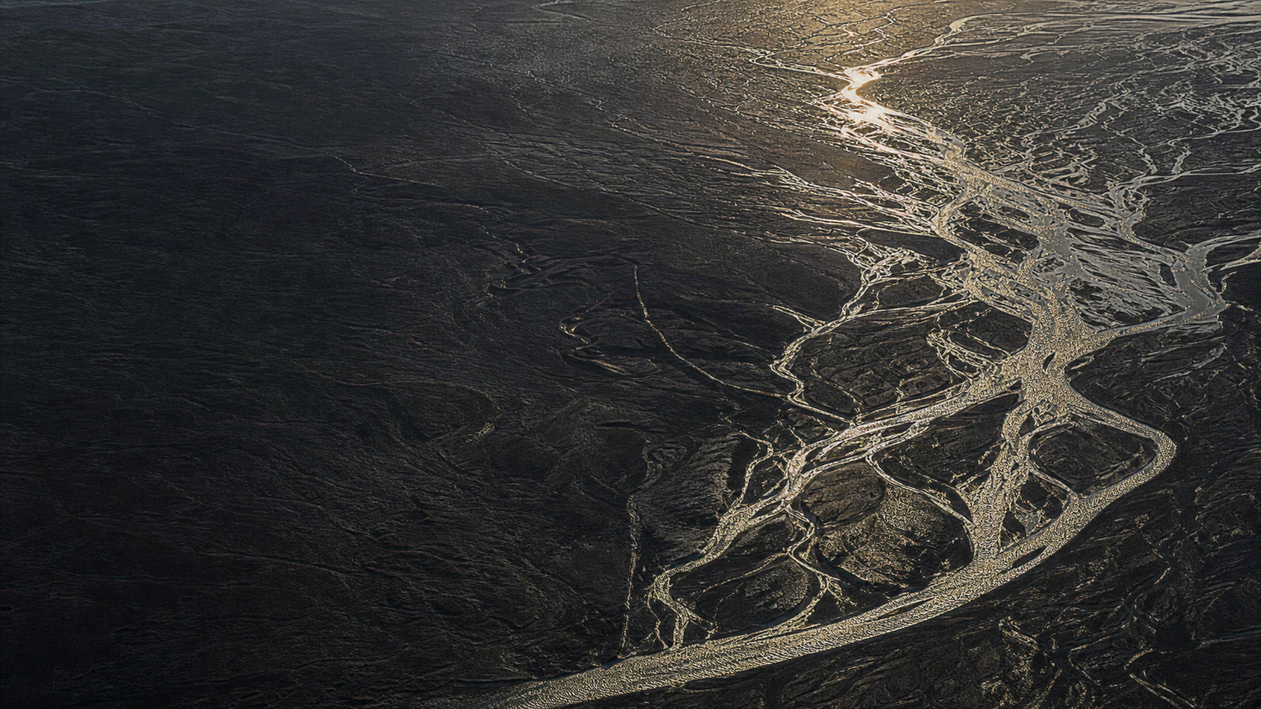 Black volcanic plain seen from high above with branching reflective gold-toned water channels, crisp sediment fans and immense scale, original 4K dark amoled wallpaper