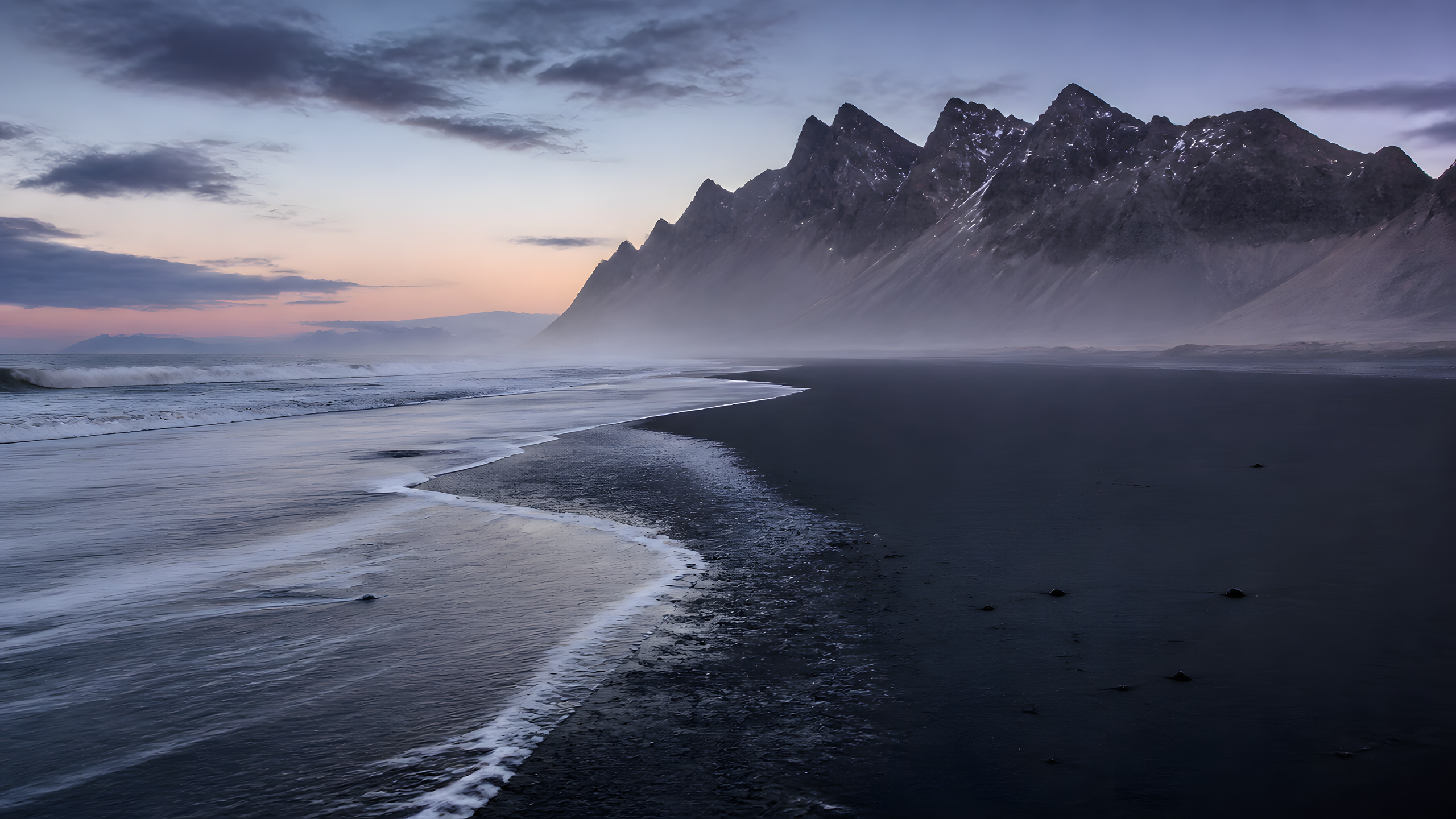 Black sand beach beneath mossy volcanic cliffs in soft dawn light, original 4K wallpaper