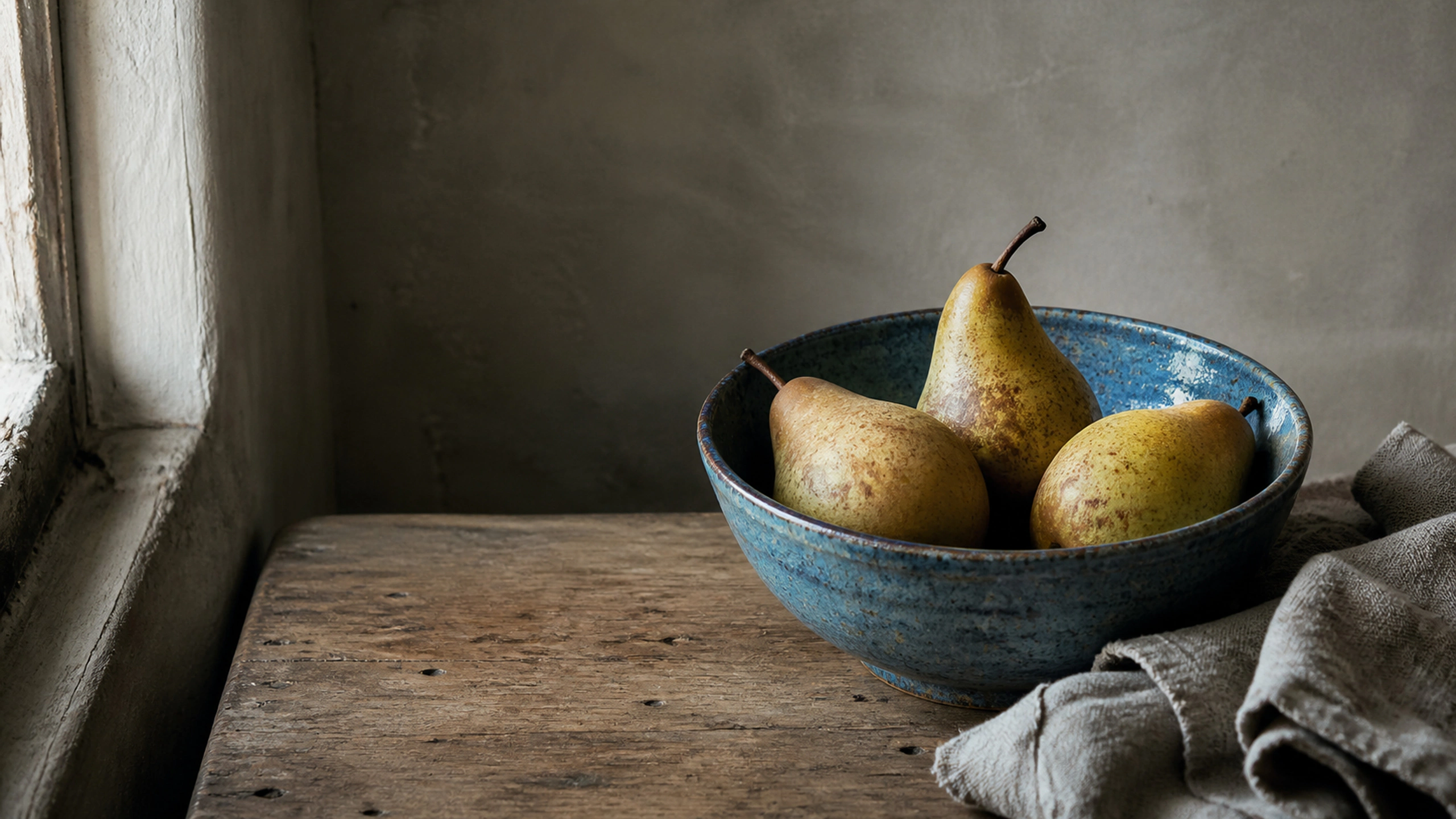 Three weathered pears in a handmade blue ceramic bowl beside folded linen, original 4K still life objects wallpaper