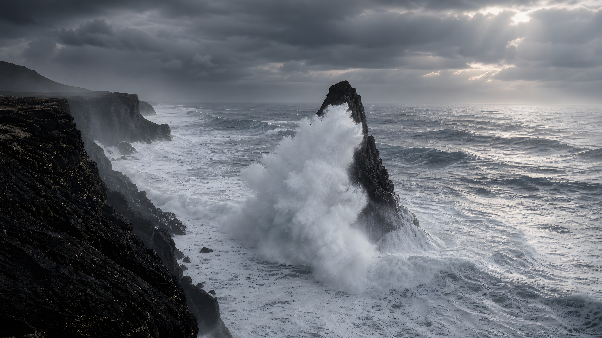 A heavy winter swell detonating against a dark basalt sea stack beneath layered storm cloud and a brief silver sunbreak, original 4K ocean wallpaper