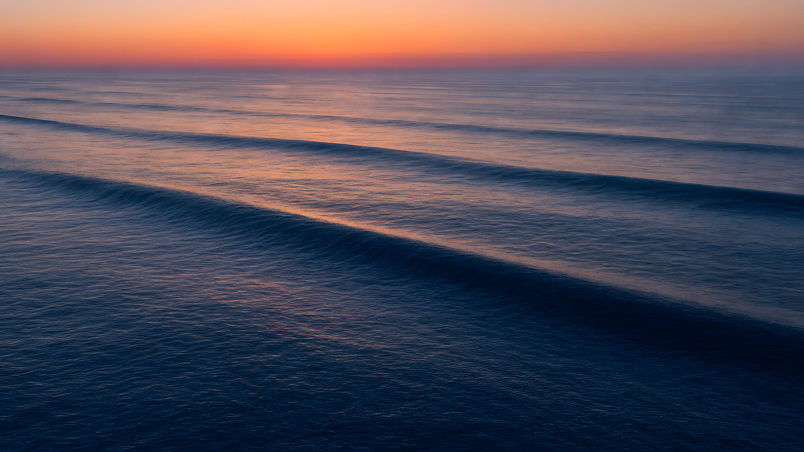 Smooth long-period ocean swells traveling in parallel across deep water at blue hour, seen from a high oblique aerial viewpoint, original 4K ocean wallpaper