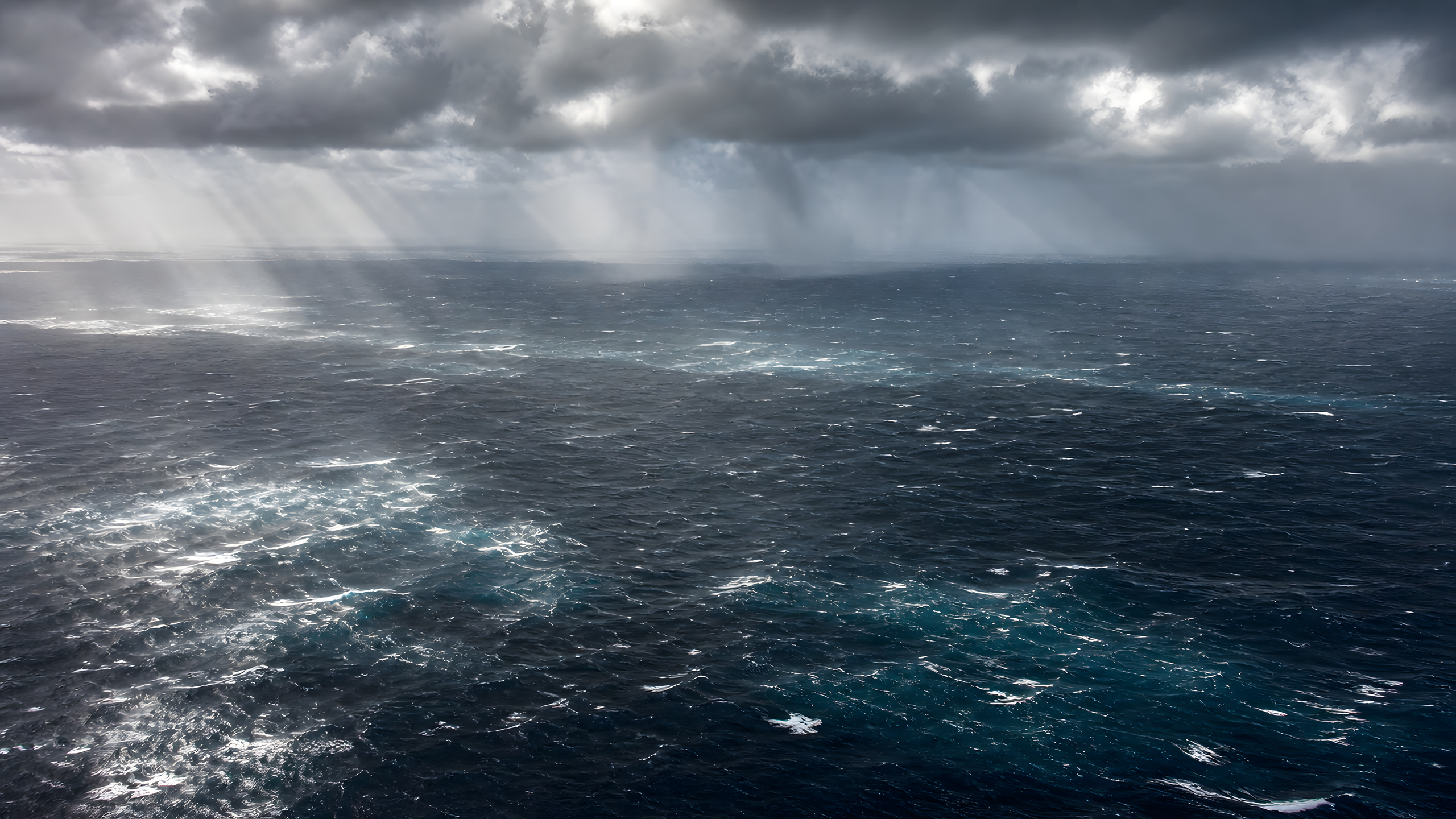 A vast windswept ocean of irregular whitecaps crossed by natural sunshafts and distant rain curtains after a storm front, original 4K ocean wallpaper