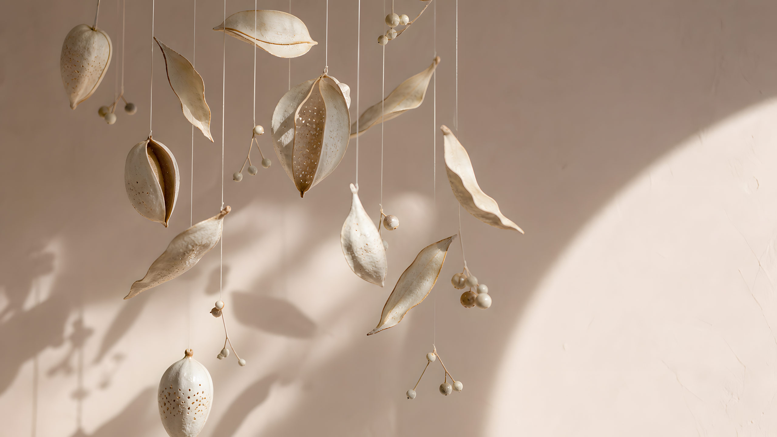An airy original mobile of translucent porcelain seed pods, curled leaves and matte ceramic berries suspended on fine linen threads against sunlit blush plaster, original 4K pastel wallpaper