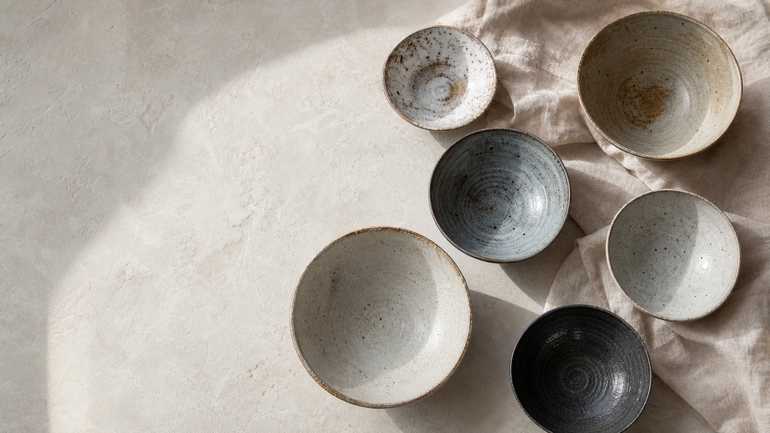 Varied wheel-thrown bowls viewed from above across a pale stone surface, original 4K still life objects wallpaper