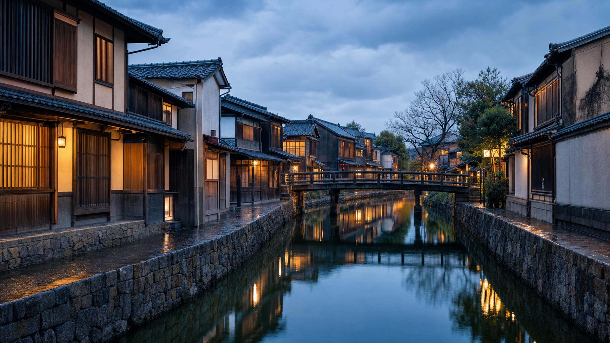 An empty canal bend lined with varied traditional timber machiya facades, stone embankments and low bridges beneath a rain-cleared blue-hour sky, original 4K travel wallpaper