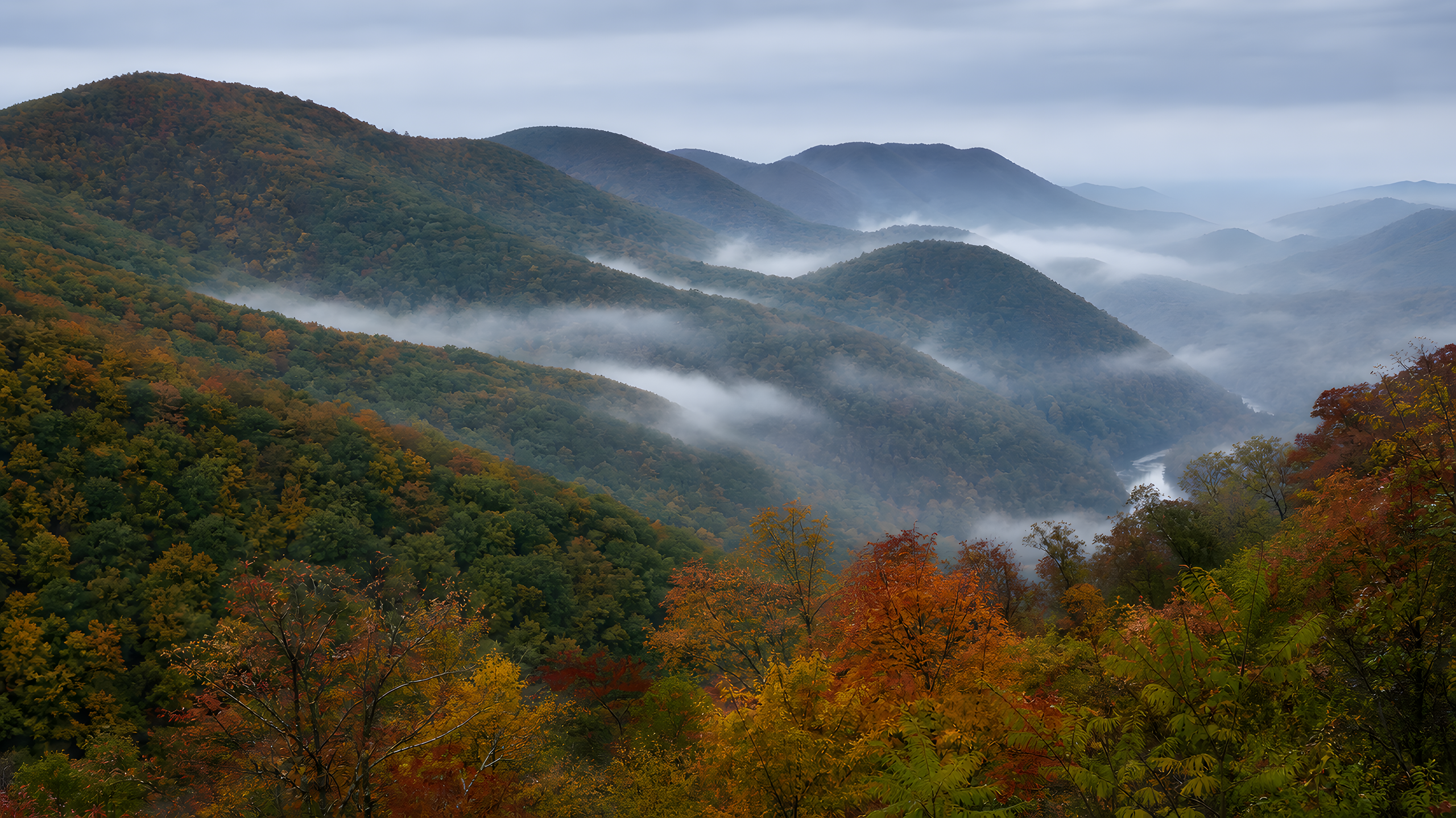 Multiple rounded deciduous mountain ridges receding diagonally through cool morning haze, with naturally transitioning autumn color, a distant silver river and fog pooled between slopes, original 4K mountains wallpaper