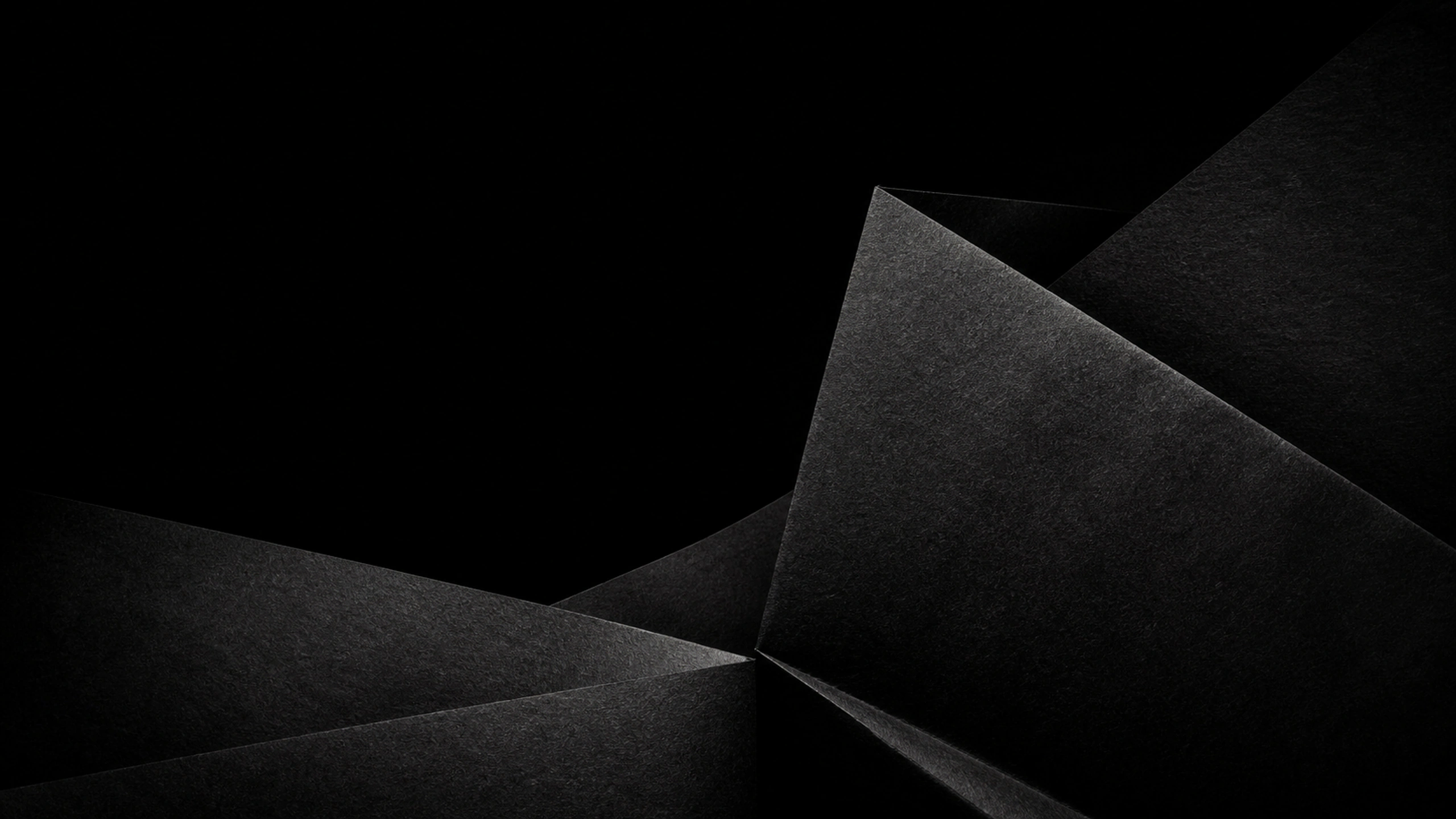 Large hand-folded black paper planes creating distinct diagonal shadow valleys, tactile fibers and one soft highlight, original 4K dark amoled wallpaper