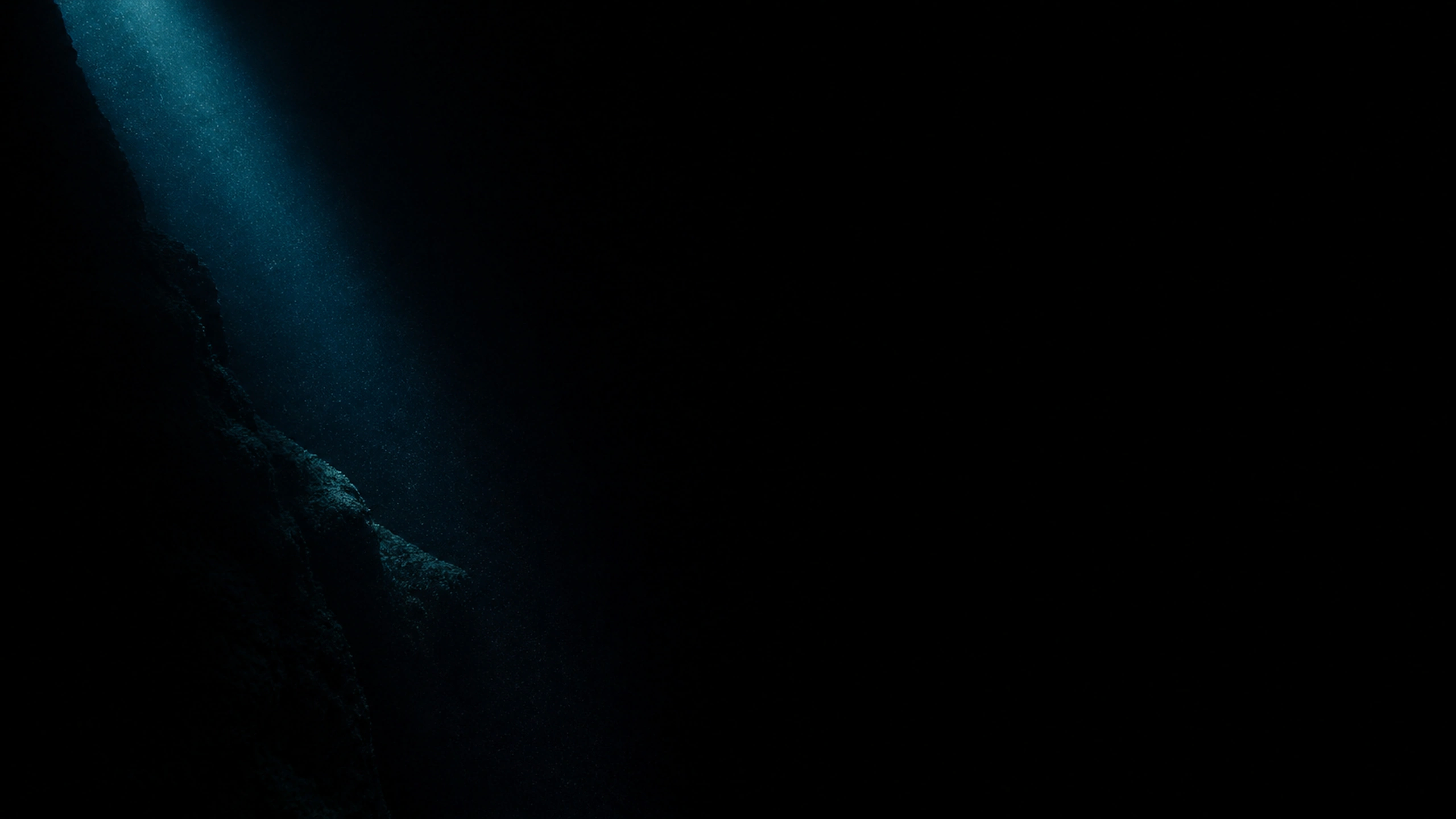 Deep black underwater void with one narrow descending surface ray revealing suspended particles and a distant rock shelf, original 4K dark amoled wallpaper