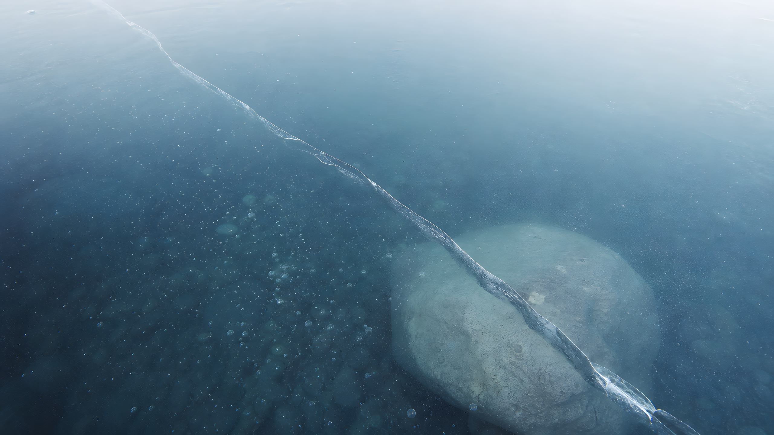 One natural hairline fracture crossing transparent alpine pond ice above a pale submerged stone, seen from directly overhead at cold dawn, original 4K minimal wallpaper
