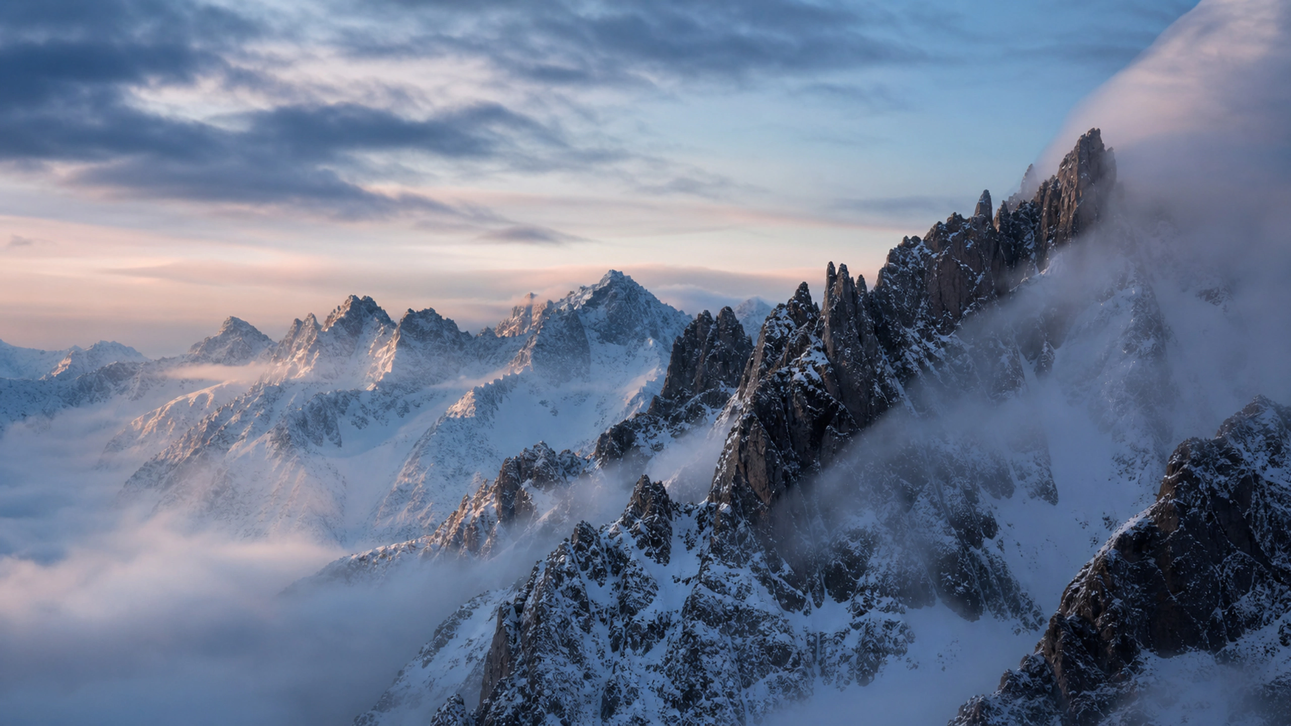 Dark granite spires rising through winter snow and high thin cloud, original 4K mountains wallpaper