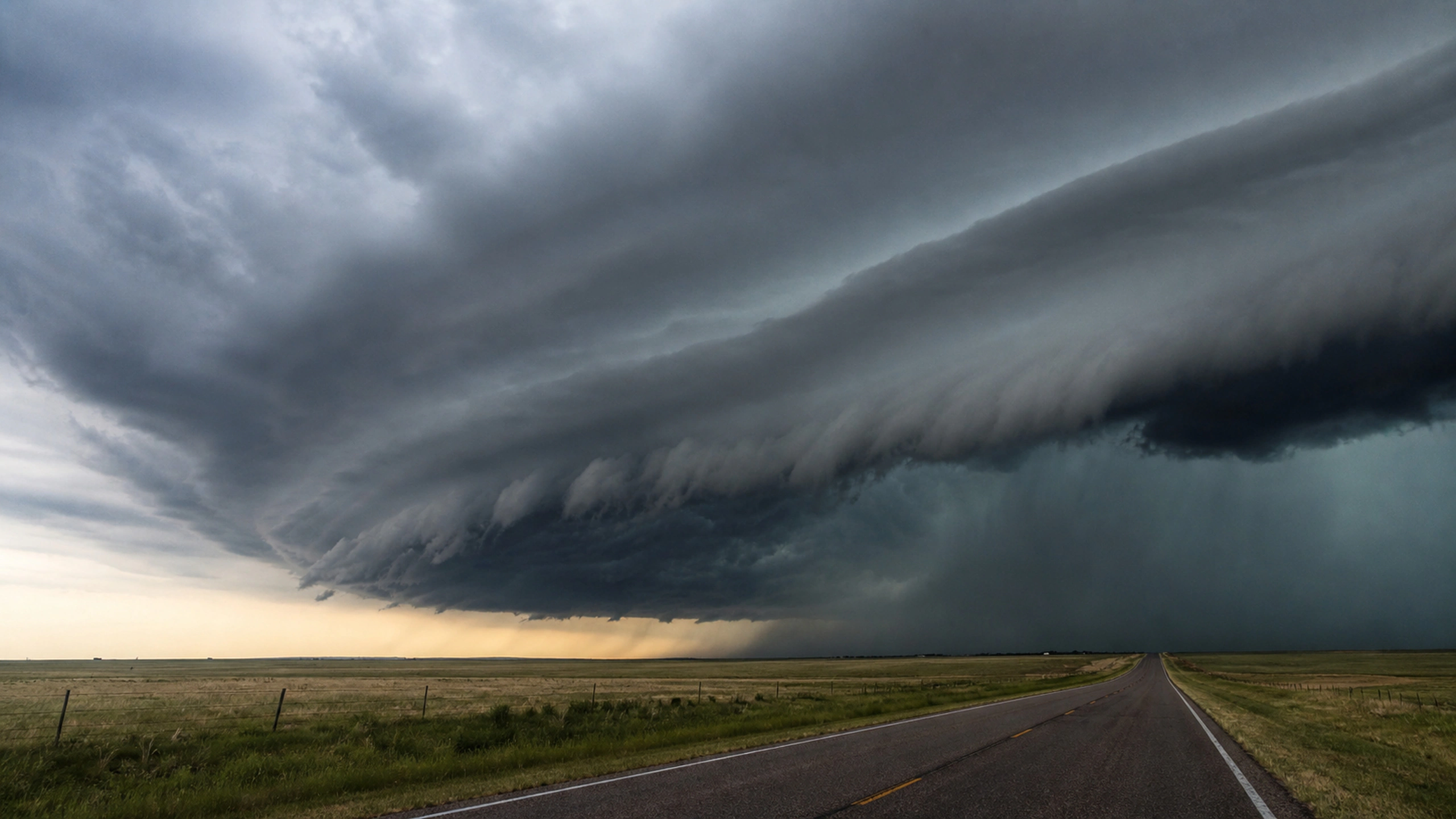 Massive shelf cloud crossing an empty straight rural road and open grassland, original 4K weather wallpaper