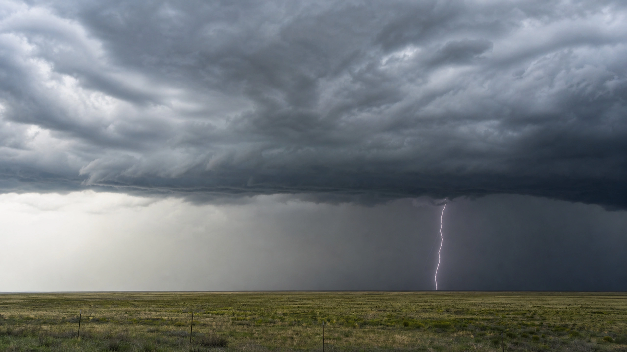 Single lightning strike beneath a layered storm seen safely across a broad plain, original 4K weather wallpaper