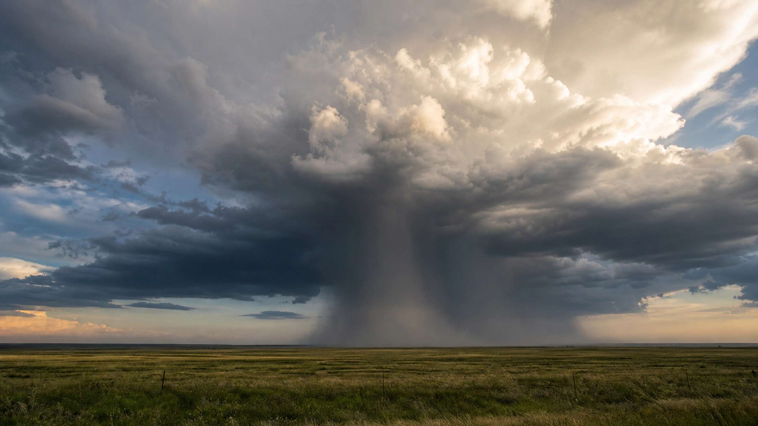 Dark visible rain core moving below a sunlit thunderhead over farmland without buildings, original 4K weather wallpaper
