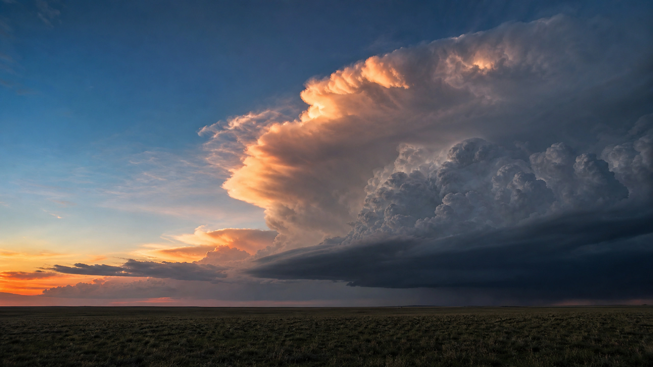 Towering storm anvil catching restrained sunset color above a dark horizon, original 4K weather wallpaper
