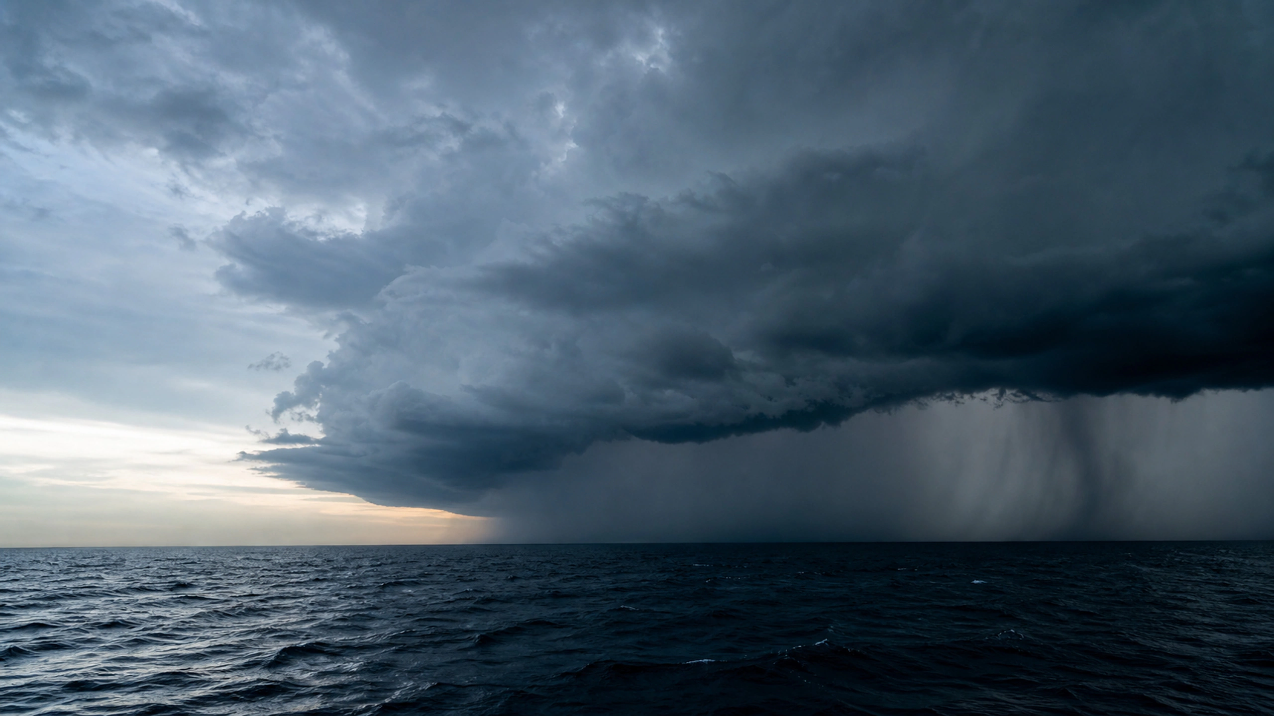 Isolated thunderstorm over a dark open sea beneath a clear distant horizon, original 4K weather wallpaper