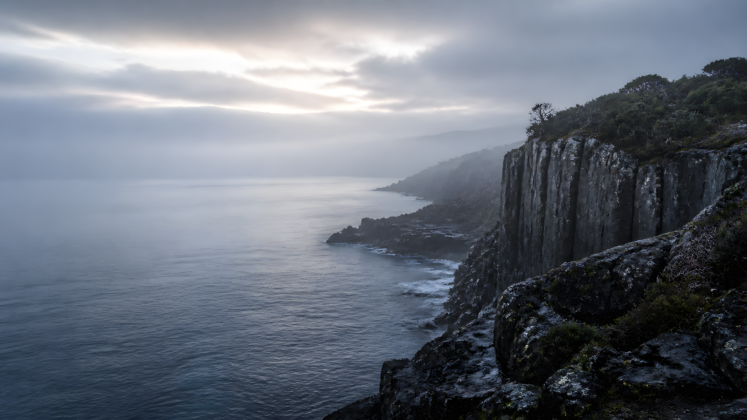 Misty basalt headland above a calm steel-blue sea at dawn